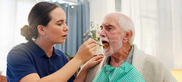 Eine Pflegedienst-Mitarbeitern reicht einem ältern Mann das Essen an
