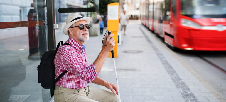 Ein Mann mit Blindenstock wartet an einer Haltestelle auf eine Straßenbahn