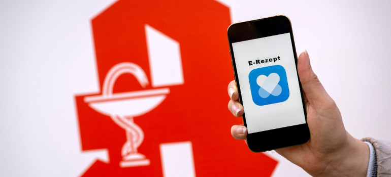 Ein Handy mit dem Logo der E-Rezept-App und im Hintergrund das Apotheken-Symbol